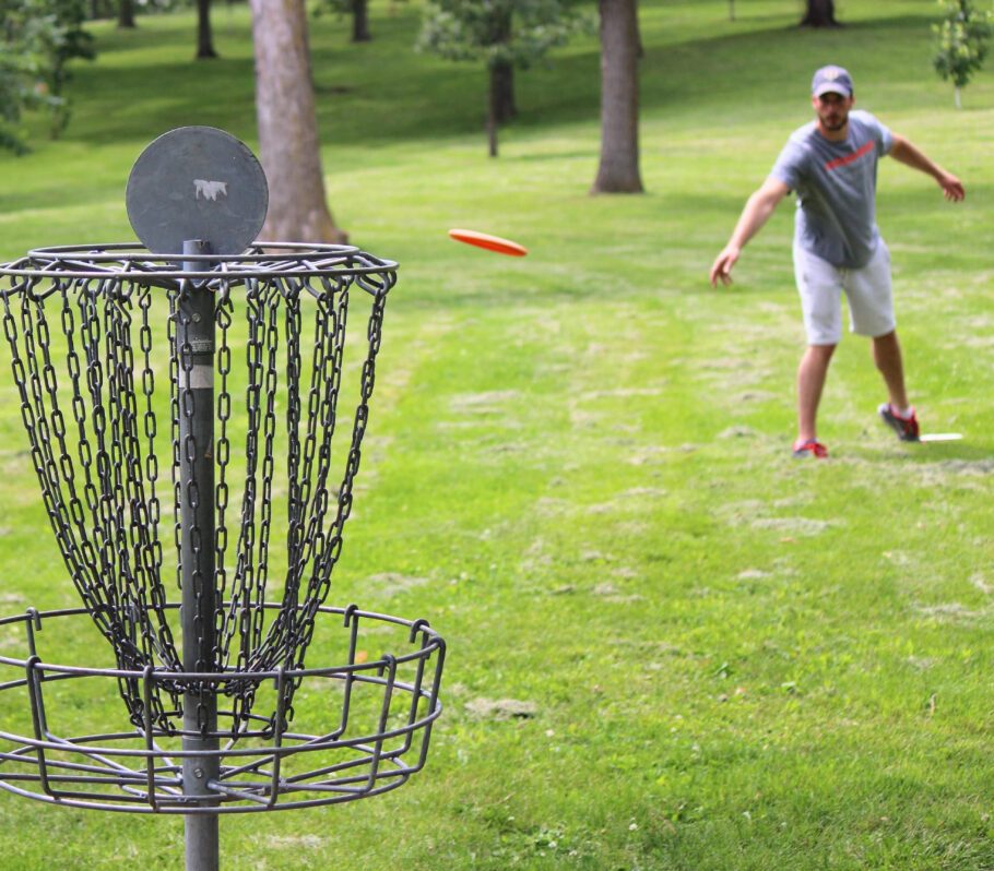 Things to do in Cashton. Community sports, such as disc golf. Image shows man throwing frisbee towards metal cage.