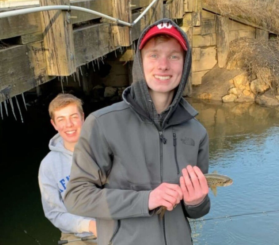 Two young men trout fishing by shore of water.