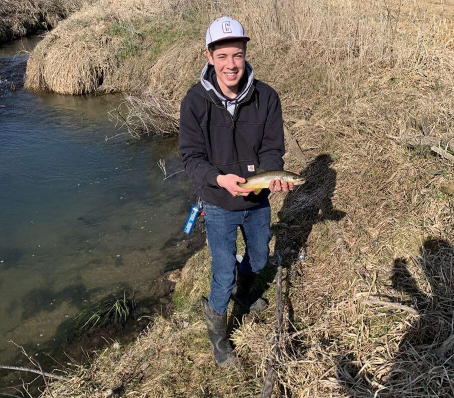 Image of young man holding trout fish that he's just caught.
