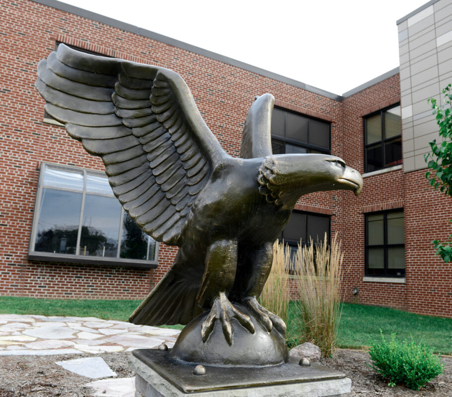 Bronze statue of eagle with wings spread open in front of building.